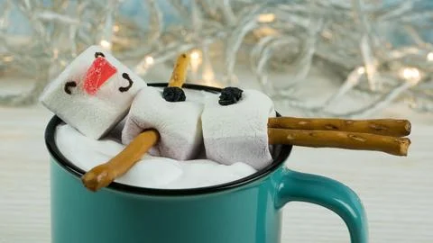 Cup of hot drink on light background. Marshmallow snowman in blue cup Stock Photos