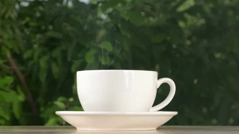 Cup of hot steaming coffee or tea on wooden table outside on green background Stock Footage 206381562