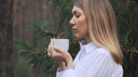 Cup of hot tea or coffee in both hands of a woman in the forest Stock Footage 82500272