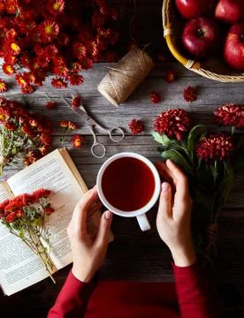 Cup of hot tea or rooibos in female hands on wooden table with flowers, book and Stock Photos