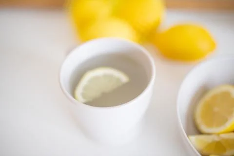 Cup of lemon tea on a white table surrounded by lemons Stock Photos