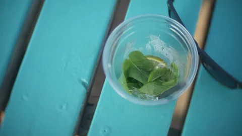 Cup with mint leaves and lemon slices on turquoise picnic table Stock Footage 341363223