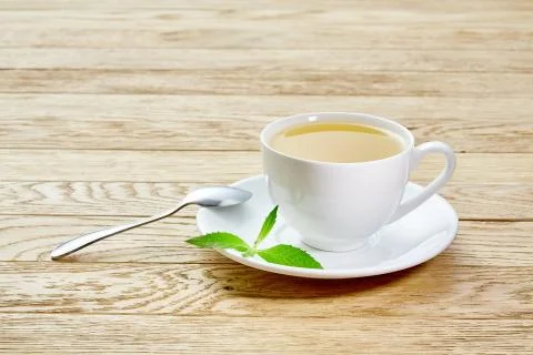Cup of mint tea and green leaves on light table Stock Photos