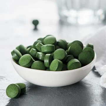 A cup of spirulina or chlorella tablets on a concrete background. Stock Photos