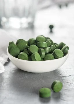 A cup of spirulina or chlorella tablets on a concrete background. Stock Photos