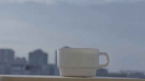 Cup of steaming beverage on balcony against sunny buildings Stock-Footage 251220448