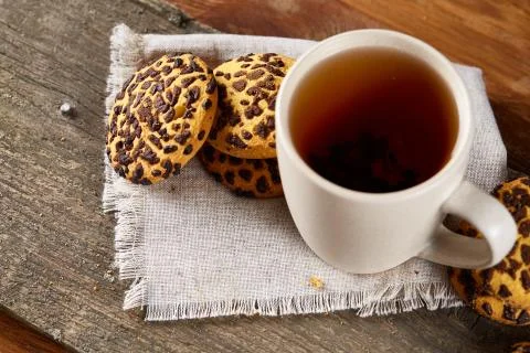 Cup of tea and chocolate chip cookies on white homespun napkin in country style Stock Photos