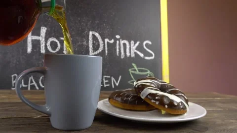 A cup of tea and donuts in chocolate glaze on a cafe table.Tea is pouring from a 스톡 동영상 145770015