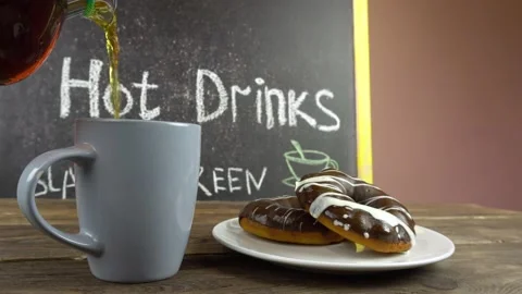 A cup of tea and donuts in chocolate glaze on a cafe table.Tea is pouring from a Stock-Footage 145831491