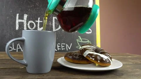 A cup of tea and donuts in chocolate glaze on a cafe table.Tea is pouring from a Stock-Footage 146239386