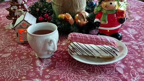 Cup of tea and plate of eclairs on Christmas decorated table. Stock Footage 225894966