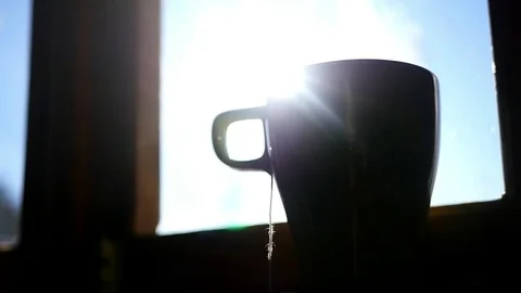 Cup of tea with a bag of standing on the window sill near the window in the rays Stock Footage 73016742