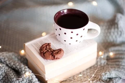 Cup of tea with chocolate cookie with bite on open books over Christmas light Stock-Fotos