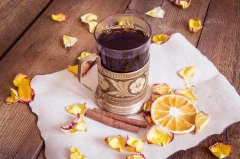 Cup of tea in coaster, dried oranges, dried rose petals on wooden background Stock Photos