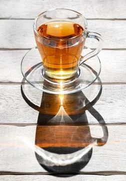 Cup of tea with contrasting shadow on white wooden table Stock Photos
