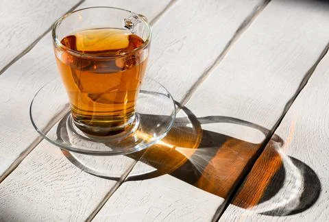 Cup of tea with contrasting shadow on white wooden table Stock Photos