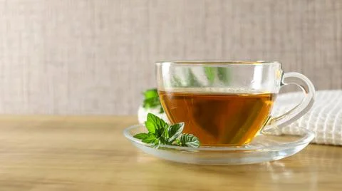 Cup of tea with fresh mint leaves on wooden table in a simple kitchen setting Stock Photos