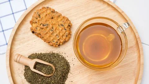 A cup of tea, green tea leaf, and cookie on a table. Stock Photos