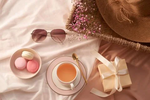 Cup of tea, macarons cake, gift box, glasses, hat and flowers on fabric backg Fotos Stock