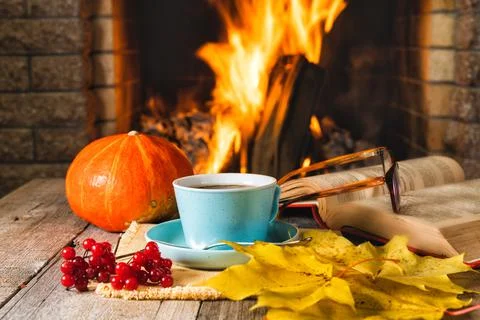 A cup of tea or coffee and yellow autumn leaves near a cozy fireplace, in a c Stock Photos