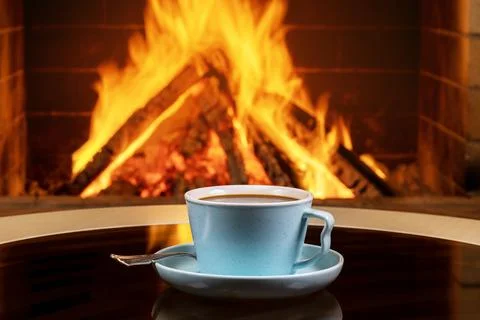 A cup of tea or coffee and old books on a background of burning fireplace. Stock Photos