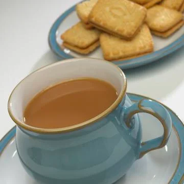 CUP OF TEA WITH PLATE OF BISCUITS IN BACKGROUND Stock Photos