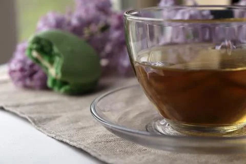 Cup of tea sits on a table next to a green dessert and lilac flowers in a bright Stock Photos
