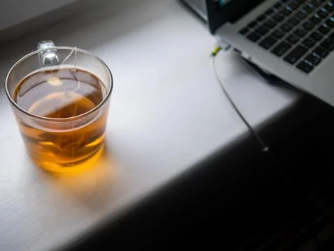 A cup of tea is sitting on a table next to a laptop Stock Photos