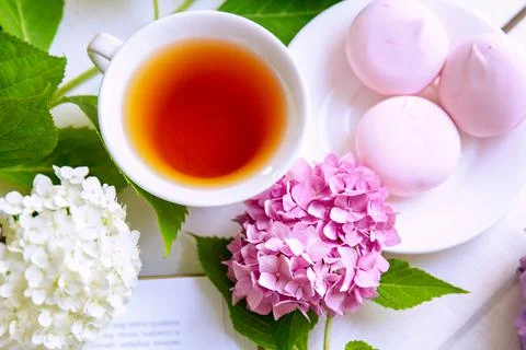 A cup of tea surrounded by hydrangea flowers, with pink marshmallows Stock Photos