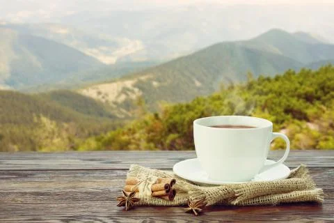 Cup with tea on table over mountains landscape with sunlight. Stock Photos