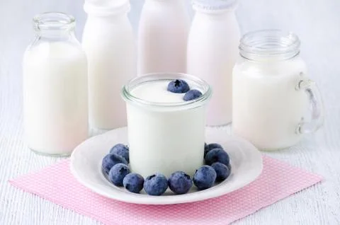 A cup of yogurt with blueberrys and different bottles of yogurt drink and milk Stock Photos