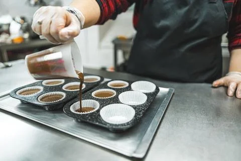 Cupcake baking. Professional pastry chef pouring chocolate batter into muffin Stock Photos