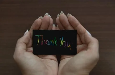 Cupped hands holding a black card with "Thank You" written in colorful rain.. Stock Photos
