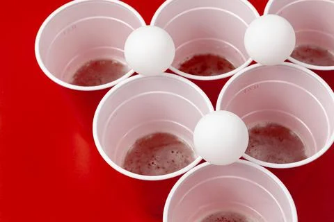 Cups and plastic ball on red background. Beer pong game Stock Photos