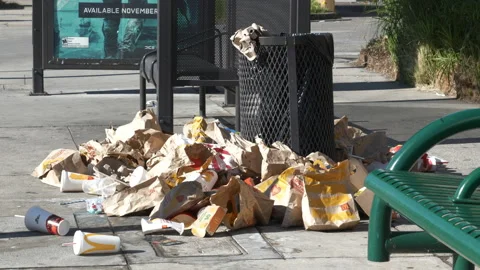 Cups blowing by a huge pile of trash at a bus stop shelter Stock Footage 165646824
