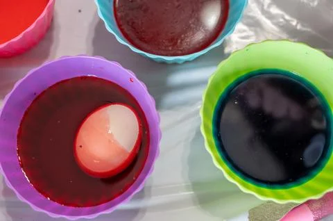 Cups of dye with an egg being lowered in for Easter decorations Stock Photos