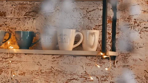 Cups on loft kitchen shelves decorated with glowing garlands Stock Footage 121980073