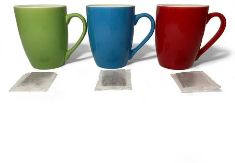 Cups stand in a row on a white background. There are tea bags next to the cups. Stock Photos