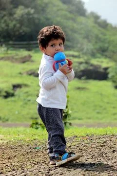 Cure boy is drinking water from his sipper. He is at a green hilly area with  Stock Photos