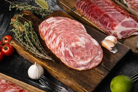 Cured italian meat Ham, prosciutto, pancetta, on black dark stone table backg Stock Photos