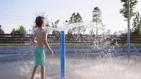 Curious 6 year old boy plays with giant water sprinkler at splash pad playground 스톡 동영상 233939790