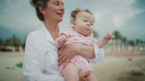 Curious baby leaning forward while being held by a mother near the shoreline, Stock Footage 337057870