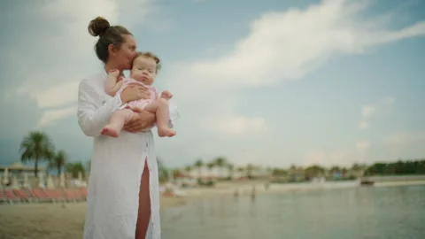 Curious baby leaning forward while being held by a mother near the shoreline, Stock Footage 337059910