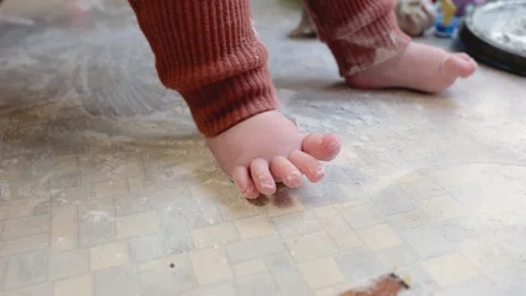 Curious baby taking first steps on a kitchen floor covered in flour, a close-up Stock Footage 346097926