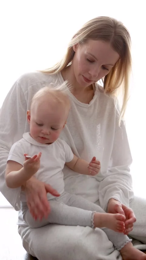 Curious baby trying put small object into mouth while attentive mother watches Stock Footage 309019578