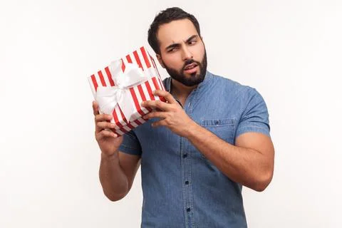 Curious bearded man shaking striped gift box trying to guess what is inside,  Stock Photos