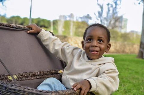 Curious black child exploring wicker basket in park: childhood adventures u.. Stock Photos