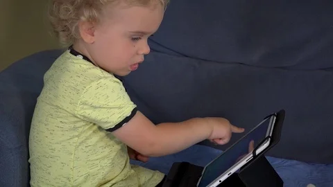 Curious blond kid touching tablet computer screen sitting on couch Stock Footage 69946665