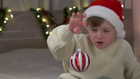 Curious boy examining red white ornament with focused expression, rotating it Stock Footage 322195567