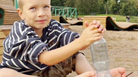 A curious boy sits barefoot and opens a water bottle. Video stock 344988338